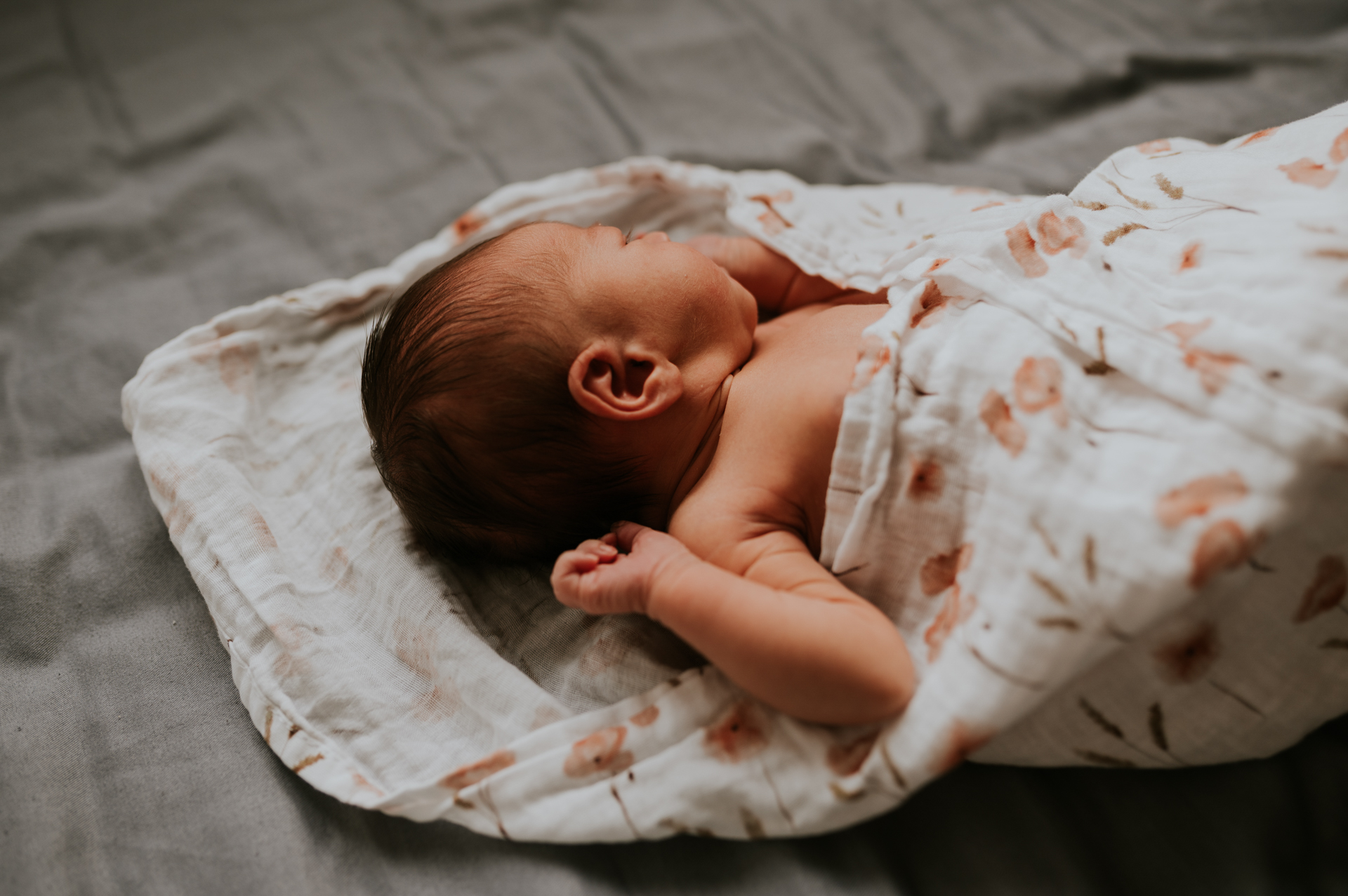 noworodek leżący na łóżku zawinięty w pieluszkę podczas zdjęć